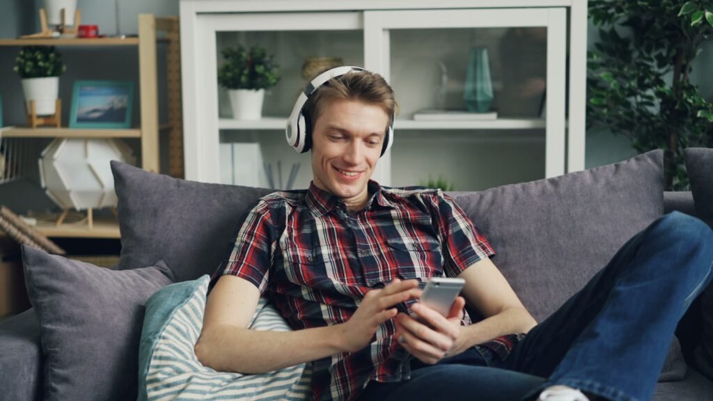 a man sitting on a couch wearing headphones and looking at a cell phone